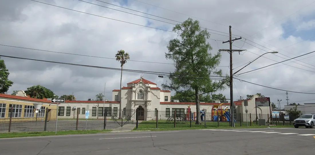 Historic white school building with red tile roof and ornate entrance behind an iron fence on Jefferson Highway