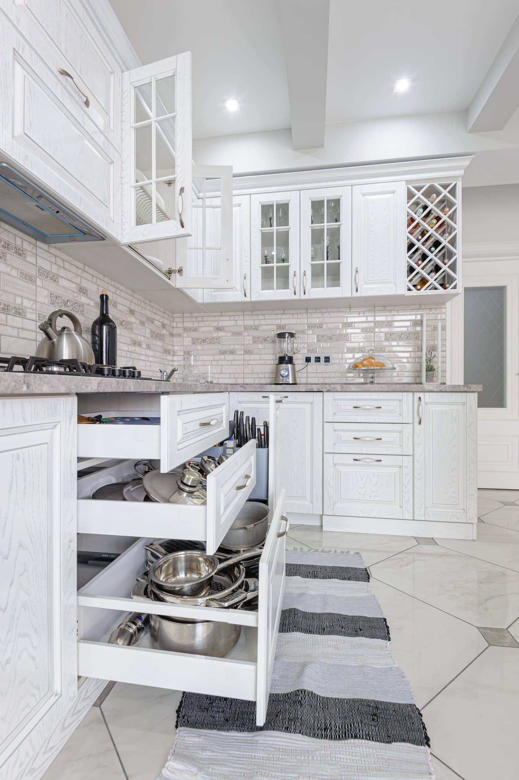 Modern kitchen with white cabinets expertly crafted through professional kitchen cabinet installation, marble walls and floor, a gas stove, open drawers, a microwave, and a wooden door in the background.