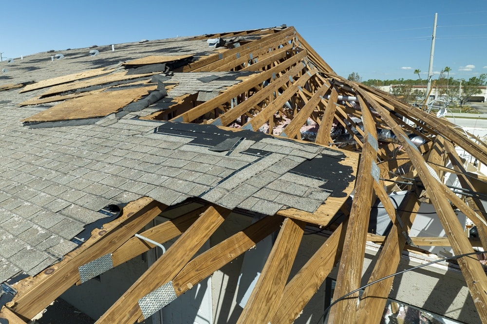 Part of a house roof is severely damaged, exposing wooden beams and missing shingles under a clear blue sky—an urgent case for expert roof repair New Orleans residents can trust.