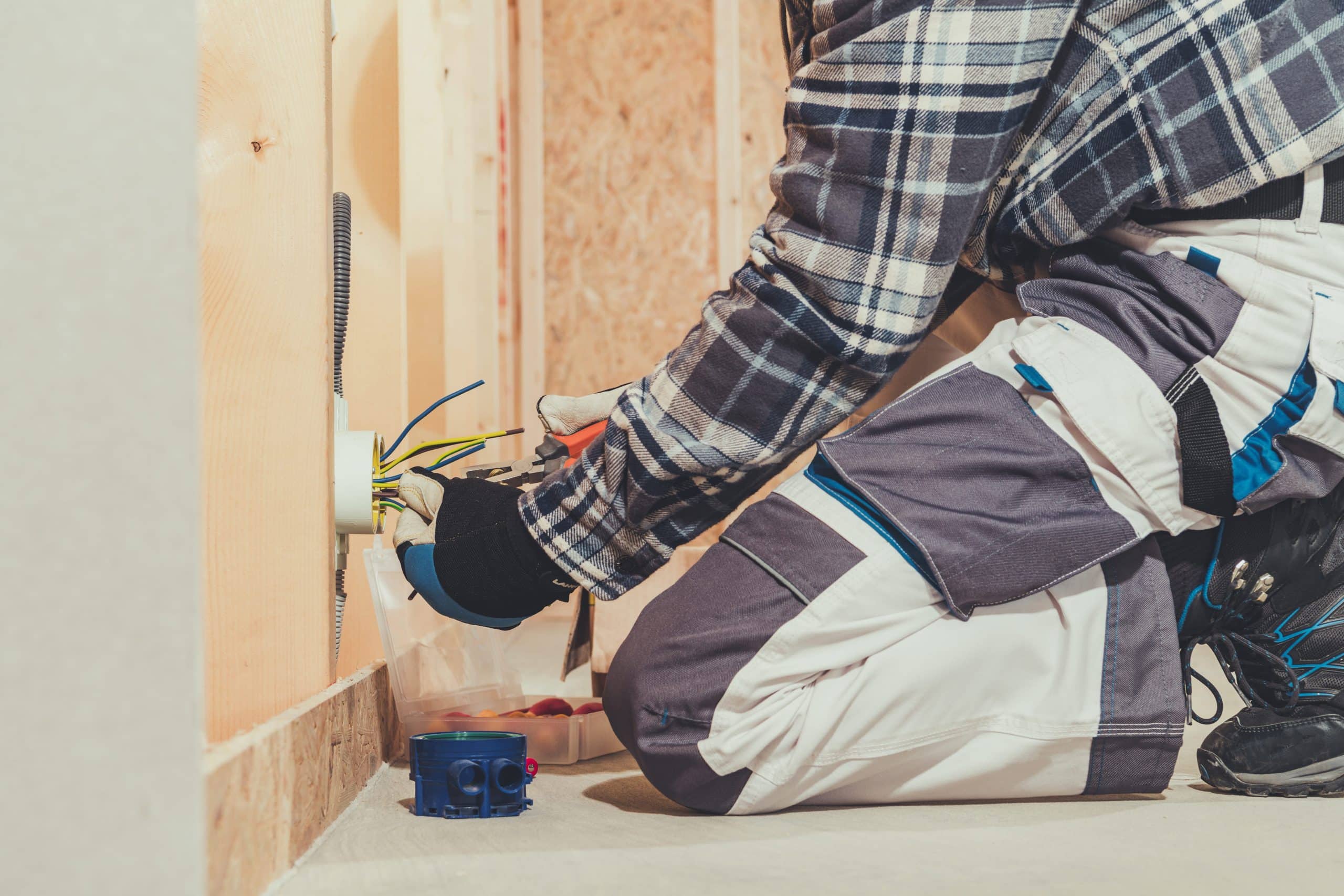 Worker wiring an outlet box low on an open stud wall before new drywall goes up