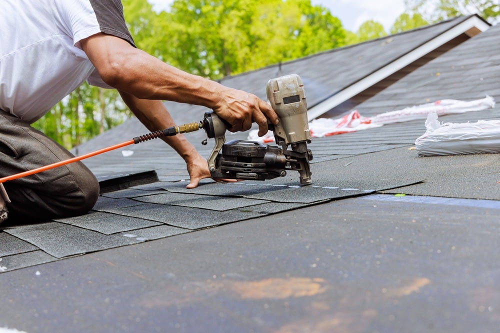 A person uses a nail gun to attach asphalt shingles to a roof during a roof repair New Orleans installation or maintenance project.