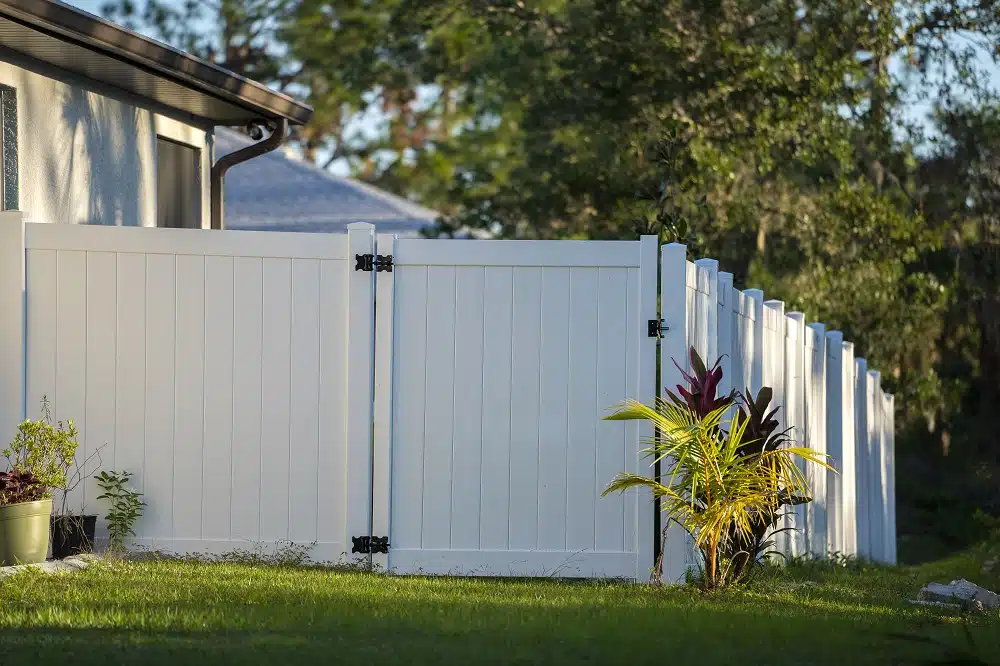 White vinyl picket fence on green lawn surrounding property grounds for backyard protection and privacy.