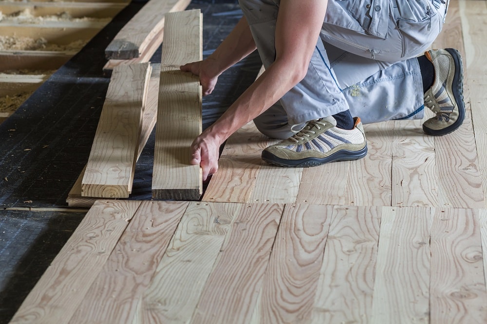 Close up of professional carpenter installing natural wooden new planks on cement floor in empty unfinished room under reconstruction. Improvement, renovation and carpentry concept.