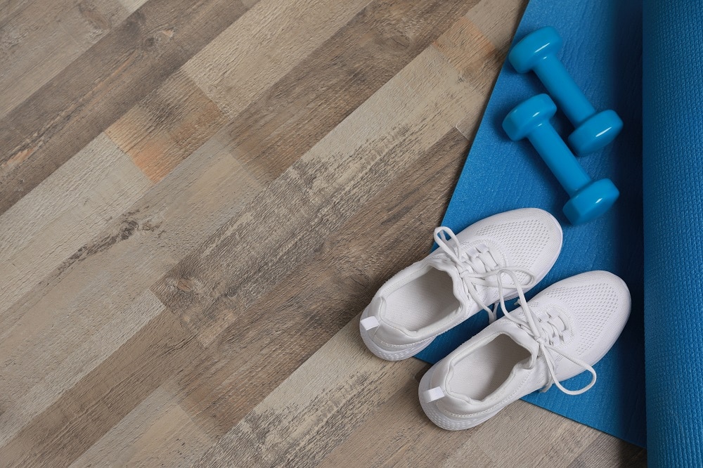 Dumbbells, sneakers and mat on wooden floor, above view. Space for text