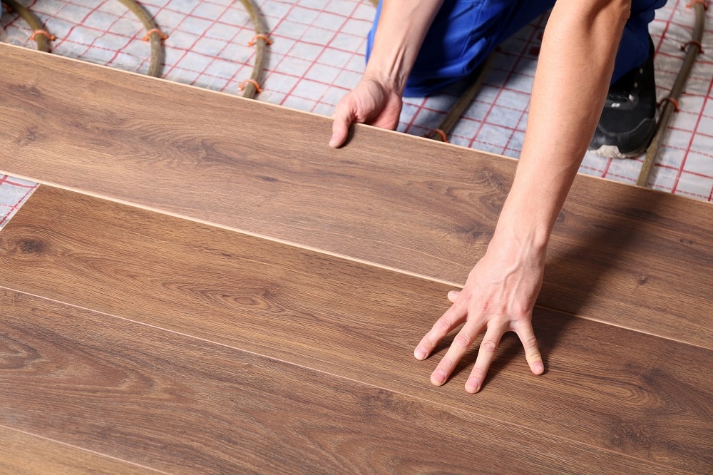Worker installing new wooden laminate over underfloor heating system, closeup
